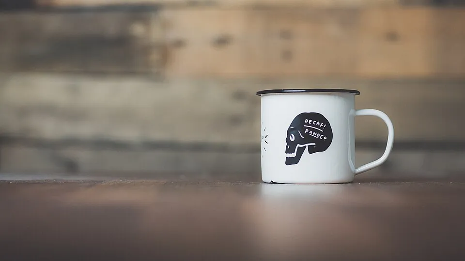 White ceramic campfire-style mug with black rim and black graphic illustration, resting on a dark wooden table